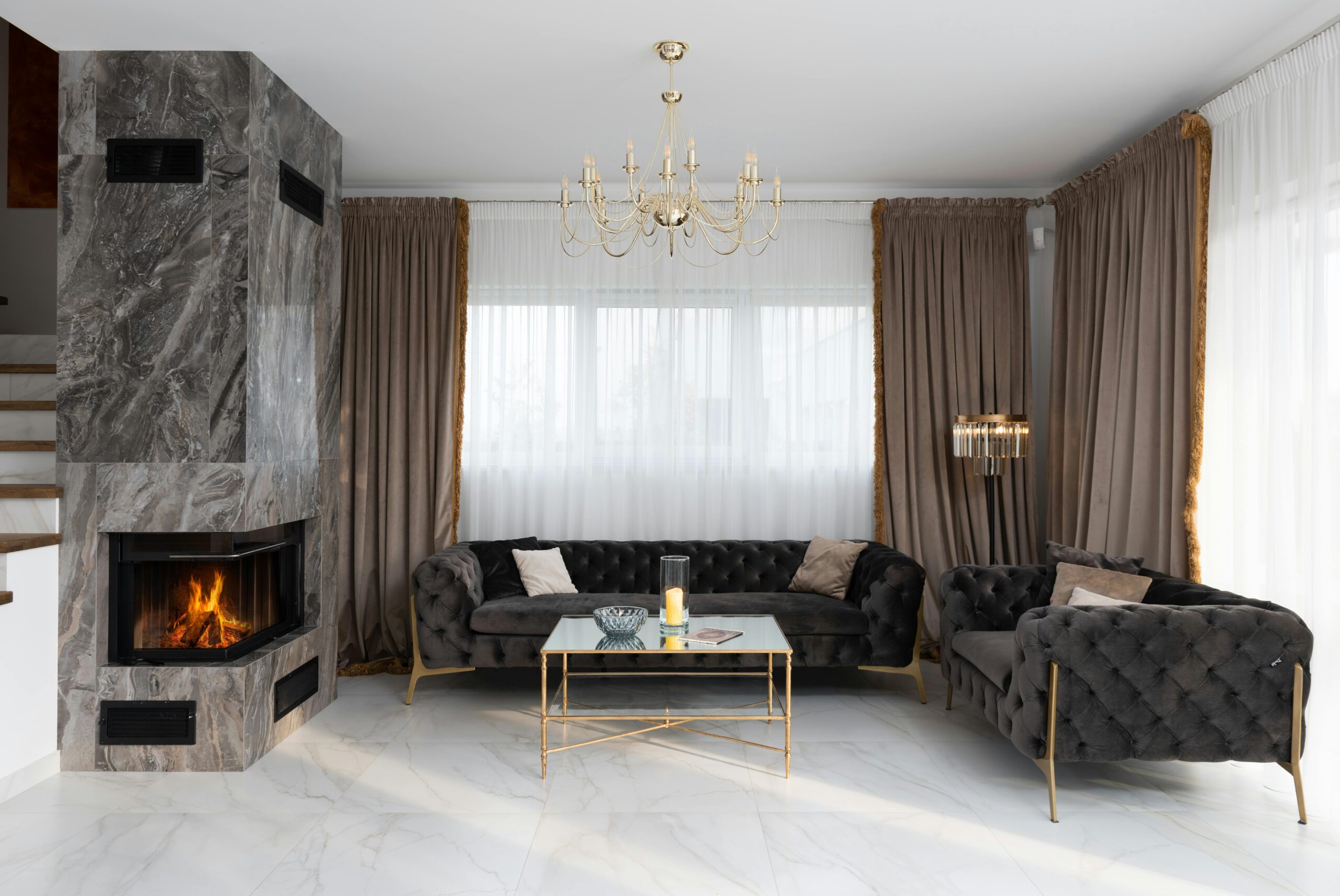 Interior of modern living room with soft couches and side table placed near windows with curtains and burning fireplace at home